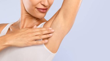 Mavi stüdyo arka planında izole edilmiş koltukaltını koklayan, elini kaldırıp Axilla 'ya dokunan mutlu kadının yakın plan görüntüsü. Ücretsiz fotokopi alanı, koltuk altı deodorantı veya epilasyon reklamı