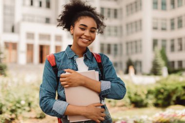 Başarılı Öğrencinin Portresi. Dışarıda modern üniversite binasının yanında duran kameraya gülümseyen mutlu Afrikalı Amerikalı genç kız poz veriyor. Öğrencilik, Modern Eğitim