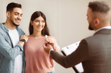 Mutlu gülümseyen Orta Doğulu çift gelecekteki yeni dairenin anahtarını alıyor. Takım elbiseli profesyonel bir emlakçı genç alıcılara anahtar veriyor. İpotek, Satılık Mülkiyet