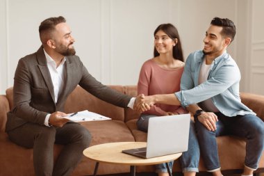 Başarılı bir anlaşma konsepti mühürleniyor. Milenyum Çifti 'nin Yeni Bir Daire Alırken Portresi, Profesyonel Emlakçıyla Tokalaşmak. Gülümseyen Takım Elbiseli Müdür Mutlu Genç Aileye Daire Satıyor
