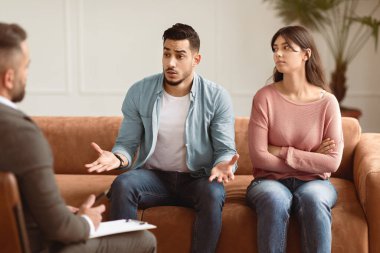 Anlaşmazlık kavramı. Koltukta oturan bir çift, mutsuz koca sorunlardan ve profesyonel evlilik danışmanı ile ayrılmaktan bahseden bir çift, katlanmış kollu bir eş. Akıl Sağlığı