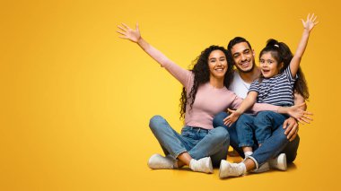 Küçük kızıyla birlikte mutlu bir Orta Doğulu ailenin sarı stüdyo geçmişinde eğlenip kaynaştığı mutlu bir portre. Olumlu Arap ebeveynler ve çocuk gülüyor ve el kaldırıyor.