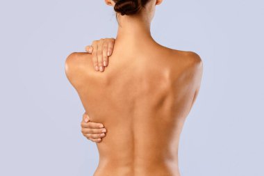 Beyaz külotlu, kendini kucaklayan, omuz ve omurgaya dokunan, masaj yapan, mavi stüdyo arka planında tek başına duran çıplak kadının arka plan görüntüsü. Güzellik Tedavisi