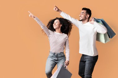 Çılgın Satış. Heyecanlı orta doğulu çift renkli alışveriş torbalarıyla havaya atlayıp sarı arka plandaki fotokopi alanını göstererek mevsimlik indirimlerden ve alışveriş anlaşmalarından ve panoramadan keyif alıyorlar.