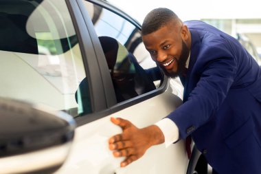 Showroom 'da yeni arabasına dokunan mutlu siyahi iş adamı, galeride dikilirken heyecanlanan Afrikalı Amerikalı erkek müşteri yeni bir araca hayranlık duyuyor.