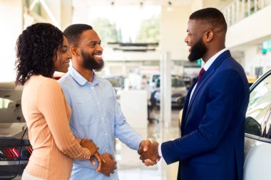 Satış Müdürü Modern Satış Merkezinde Siyah Çiftin Yeni Araba Seçmesine, Başarılı Bir Anlaşmadan Sonra El sıkışmasına, Afro-Amerikan Eşlerinin Araba Dükkanında Aile Aracı Almasına, Kapanış