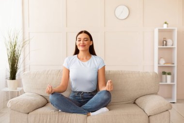 Ev Yogası. Lotus pozisyonunda meditasyon yapan sakin bir kız. İçerideki koltukta dinleniyor. Metin için Boş Alan