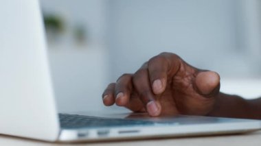 Genç bir Afro-Amerikan adam dizüstü bilgisayarına odaklanmış, rahat evindeki teknolojiyle yakından ilgileniyor. Atmosfer rahatlamayı ve modern cihazlarla bağlantıyı gösteriyor..