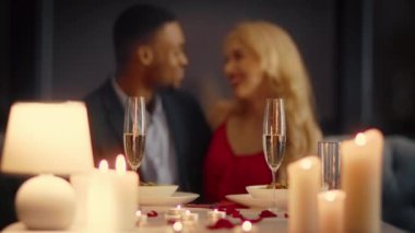 Çeşitli bir çift, mum ışığı ve güzel dekorlarla çevrili bir restoranda samimi bir akşam yemeğini paylaşıyor. Sevecen gülümsemeleri bu özel gecede paylaştıkları sevgiyi gösteriyor..