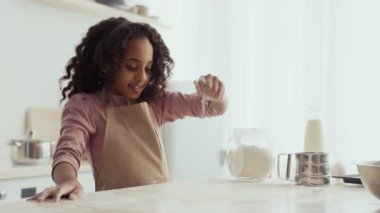 Kız, ev mutfağında yaratıcı pişirme sürecinin tadını çıkarırken un serpiyor.