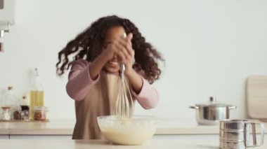 Genç kız enerji dolu bir şekilde hamur çırpıyor. Etrafı malzemelerle ve mutfak gereçleriyle çevrili..