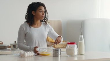 Bir kadın mutfakta yemek tarifi için yumurta çırpmakla meşgul. Etrafı çeşitli malzemelerle çevrili temiz bir tezgahta duruyor. Mutfak becerilerini ve yaratıcılığını sergiliyor..