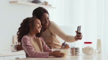 Neşeli bir anne ve kızı mutfakta özel bir anı paylaşıyor, gülümsüyor ve birlikte yemek pişirirken bir anıyı yakalıyorlar. Evlerinde sevgi ve sıcaklıkla tatlılar yaratırlar..