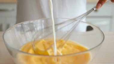 Parlak bir mutfakta bin yıllık Afro-Amerikan bir kadın cam bir kâsede malzemeleri karıştırıyor, güneşli bir öğleden sonra evde yemek pişirme ve pişirme tutkusunu sergiliyor..