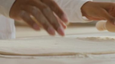Bir kadın, parlak ve davetkar bir mutfakta un kaplı bir yüzeye ustalıkla hamur döker. Yemek pişirmeye olan tutkusu, bir sonraki aşçılığını dikkatlice hazırlarken belli oluyor..