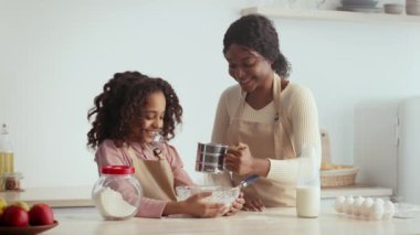 Bir anne ve kızı kendi evlerinin mutfağında neşeyle yemek pişirir. İçindekileri ölçüp pasta hazırlıyorlar, kahkaha ve sevgiyle dolu bir anı paylaşıyorlar..
