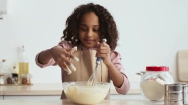 Kız çırpıcıyla bir kase karıştırıyor, sıcak ev mutfağında özel anılar yaratıyor, hamur işi pişiriyor.
