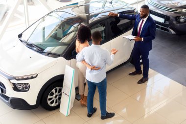 Profesyonel satıcı, Showroom 'da siyahi müşteriler için yeni araba reklamı yapıyor, Afro-Amerikan eşler aile otomobili alırken müdürle konuşuyor, galeri merkezinde, Top View' da.