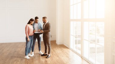 Uzmanlarla istişare. Gülümseyen genç çift emlakçı ya da komisyoncuyla anlaşma yapmak için sözleşme detaylarını tartışıyor. Toplantıda müşterilerle konuşan profesyonel mali danışman ya da satıcı