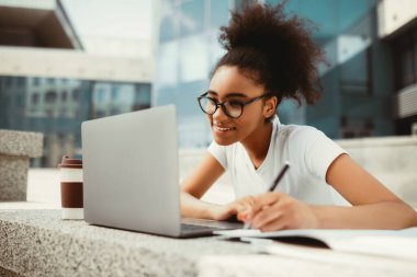 Mutlu Siyahi Öğrenci Ödev Yapıyor Laptop kullanarak Not alıyor Çevrimiçi Ders İzliyor Modern Üniversite Binası 'nın yanında oturuyor. Modern Uzaktan Eğitim, E-Öğrenim ve Öğrencilik