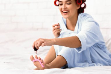 Bukleli neşeli kız çivi çakıyor. Pedikür yapıyor. Kapalı bir odada oturuyor. Evde güzellik günü. Seçici Odaklanma, Boşluk Boşluğu