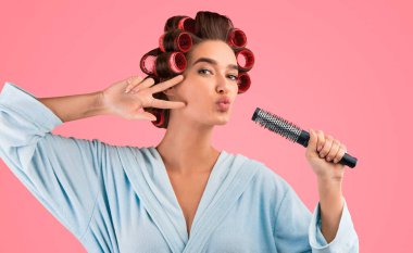 Sarı Stüdyo 'nun arka planında saç fırçasıyla eğlenceli pozlar veren kıvırcık saçlı ve stil sahibi bir kadın. Saç Bakımı ve Saç Tarzı Konsepti.