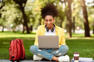 E-öğrenme. Çevrimiçi Uzaktan Konferans Veren Afro-Amerikan Üniversiteli Kız Parkta Çimlerde Oturuyor. Bilgisayar Uzaktan Öğrenme yoluyla İnternet Taraması yapan Bayan Öğrenci