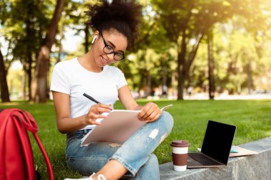 Siyahi Öğrenci Kız Çizim Yapıyor ya da Not Alıyor İnternette, Kampüs Parkı 'nın dışında dizüstü bilgisayarla oturuyor, Derse hazırlanıyor. Eğitim ve E-Öğrenim