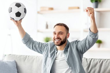 Heyecanlı genç adam TV 'de futbol seyrediyor, topu kafasının üstüne kaldırıyor, evdeki koltukta gol ya da zaferi kutluyor. Mutlu milenyum adamı favori futbol takımını destekliyor, şampiyonluğu seyrediyor.