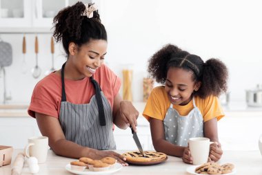 Heyecanlı siyah anne ve kız önlüklü ev yapımı çilekli turta tatma, pasta kesme ve gülümseme, mutfak içi. Mutlu Afro-Amerikan anne ve çocuk evde birlikte yemek pişiriyor, boşluğu kopyalıyor.