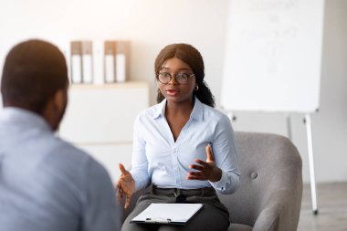Psikolojik danışmanlık. Profesyonel kadın psikoterapist ofiste genç siyahi bir adamla seans yapıyor. Afrika kökenli Amerikalı danışman, akıl sağlığı kliniğindeki bin yıllık adama danışmanlık yapıyor.