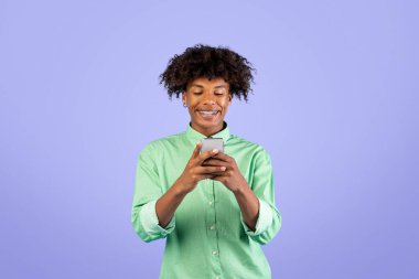 İnsanlar ve aletler. Mutlu siyah adam akıllı telefon kullanıyor, gülümsüyor, internette geziniyor ve sosyal medyada mavi stüdyonun arkasında duruyor.