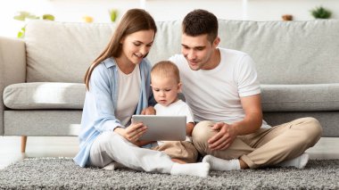 Aile eğlencesi. Millennial anne ve baba, evde dijital tablet kullanan tatlı çocuklarıyla birlikte, küçük çocukla oturma odasında dinlenirken, mutlu genç ebeveynler modern Gadget kullanıyorlar.