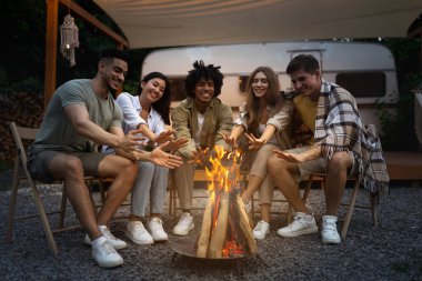 Açık hava eğlencesi. Milenyum çeşitliliği olan arkadaşlar ateşin yanında oturuyor, el ısıtıyor, geceleri birlikte eğleniyor, karavanda seyahat ediyor, arkadaşça sohbetin tadını çıkarıyor.