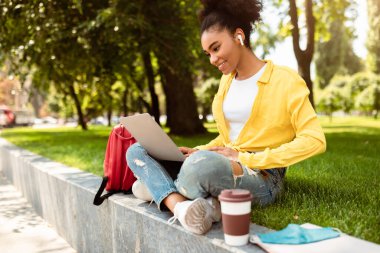 Bilgisayarlı başarılı Afrikalı Amerikalı Öğrenci Kız Bilgisayar Öğreniyor ve Kulaklık takan Kulaklıklar Giyiyor Video Çağrısında veya Açık Hava Sınıfı 'nda