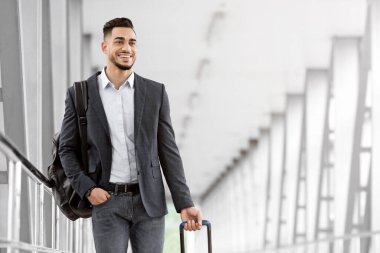 Yolculuk için hazır. Havalimanı Terminali 'nde bavulla dolaşan yakışıklı bir Arap, uçuş kapısına giderken yanında bavulunu taşıyan gülümseyen genç bir Orta Doğulu.
