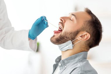 Kadın doktor klinikteki genç adam için oral koronavirüs PCR testi yapıyor. Millennial adam covid tanı prosedüründen geçiyor. Bulaşıcı hastalıkların önlenmesi ve korunma kavramı