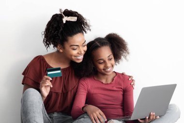 Mutlu siyah anne ve genç kız çevrimiçi alışveriş yapıyor, evde duvarda boş boş oturuyor, kredi kartı tutuyor ve modern dizüstü bilgisayar kullanıyor, internetten sipariş veriyor, kapatıyor.