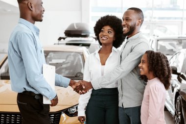 Afro ailenin araba satıcısıyla el sıkışması, galeride otomobil satın alma anlaşması yapması. Siyah veliler ve kızları otomobil galerisinden yeni bir araç alıyorlar.