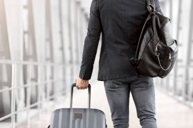 Sırt çantalı ve bavullu tanımlanamayan erkek gezgin havaalanında yürürken, genç adamın uçuş kapısından geçerken arkadan görüntüsü, kopyala...