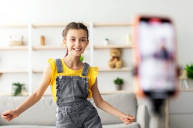 Genç blog yazarının portresi, kamera önünde dans eden, tripoda telefon kullanan, sosyal medyada paylaşmak için mobil uygulamalarda trend içeriği yaratan, seçici odak noktası olan özel videolar çekiyor.