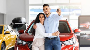 Mutlu, güzel, Müslüman bir aile babası genç bir adam ve uzun saçlı bir kadın salonda yeni bir araba satın alıyor, kırmızı lüks otomobilin başında duruyor, yeni arabalarının anahtarlarını gösteriyor ve sarılıyorlar.
