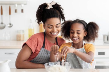 Neşeli Afro-Amerikan anne ve kızı evde birlikte kurabiye yapıyorlar, önlük giyiyorlar, hamur işlerine un ekliyorlar, birlikte iyi vakit geçiriyorlar, kek pişiriyorlar, mutfak içleri, fotokopi çekiyorlar.