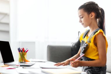 Online Eğitim Konsepti. Evde okuyan, defterine ya da günlüğüne yazı yazan, ödev yapan ya da boş ekranlı dizüstü bilgisayar kullanan bir kızın profil yan görüntüsü