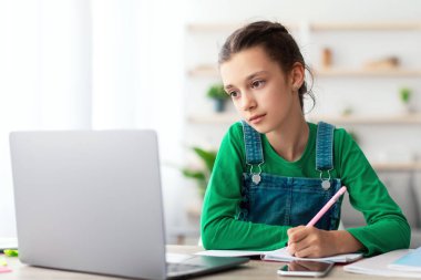 Web tabanlı Uzaklık Eğitim Konsepti. Oturma odasında oturan çalışkan gencin portresi dizüstü bilgisayarındaki yazıya bakarak. Liseli kız çevrimiçi ders izliyor, notlar alıyor.