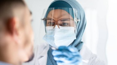 Türbanlı İslami Diş Hekimi Kadın Koruyucu Tıbbi Maske Giyiyor ve Yüzü Koruyucu Kalkan Denetleme Hastaları Dişleri, Müslüman Stomatolog Kadın Diş Kliniğinde Genç Adam İçin Kontrol Yapıyor, Kapatma
