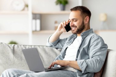 Akıllı telefondan konuşan çekici bir genç ve ofisteki koltukta dizüstü bilgisayar kullanan biri. Yakışıklı erkek işadamı müşterisiyle telefon görüşmesi yapıyor, taşınabilir bilgisayar üzerinde çalışıyor.