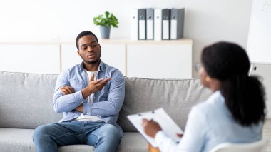Depresyon tedavisi ve duygusal bozukluklar. Profesyonel psikolog zenci erkek hastaya yardım ediyor, mutsuz Afrikalı Amerikalı bir adamla çalışıyor, klinikte destek ve yardım sağlıyor.