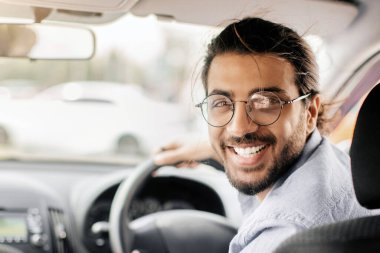 Neşeli orta doğulu genç taksi şoförü arka koltuğa bakıyor ve kameraya gülümsüyor, yakın plan fotoğraf, fotokopi odası. Mutlu Arap adam yeni arabasının tadını çıkarıyor, test sürüşü yapıyor.