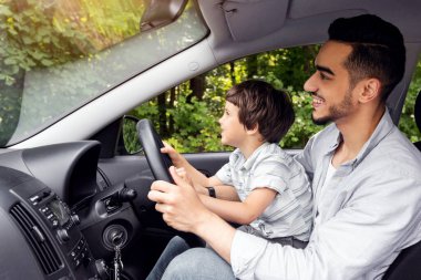 Happy smiling muslim young male teaches small kid how to drive, profile. Dad and son got drive lesson, new car, auto safety, life insurance, study at free time together. Love and family relationships